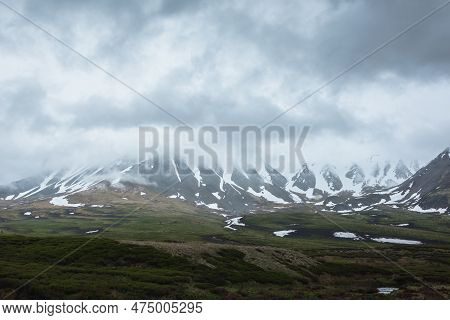 Dramatic Alpine Landscape With Snowy Mountains In Gray Low Clouds. Bleak Atmospheric Scenery Of Tund