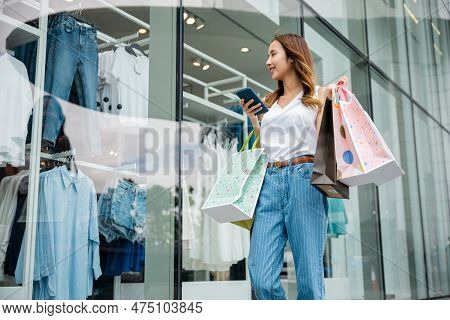 Asian Beautiful Woman Holding Shopping Bag And Smartphone On Her Hands Looking To The Mall Shop Wind