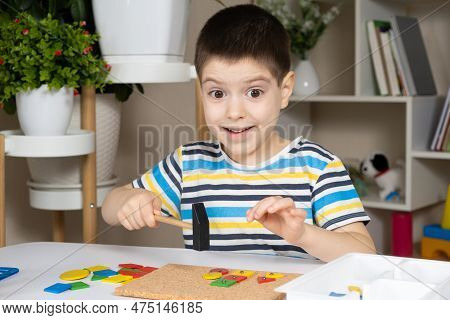 A Preschool Child Plays With A Mosaic, Builds Figures On A Board, Hammering Nails With A Hammer On M