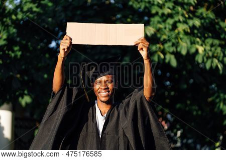 Portrait Of Smiling Black Guy Standing With Upraised Empty Cardboard Poster On Street Looking For Jo