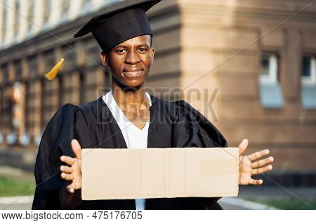 Poor Black Guy Standing With Cardboard Sign On Street Looking For Job. University Or College Graduat