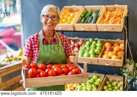 Mature Woman Works In Fruits And Vegetables Shop. She Is Holding Basket With Tomatoes.