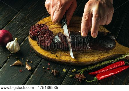 Close-up Cook's Hands With A Knife Cut Blood Sausage On A Kitchen Cutting Board. Cooking A National 