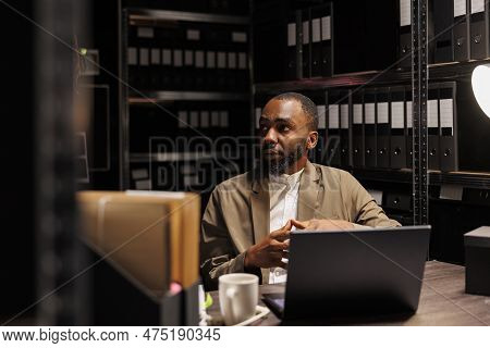 African American Policeman Working With Archival Crime Case Files And Searching Information On Lapto
