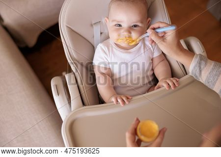 High Angle View Of Mother Feeding Cheerful Baby Boy With Porridge, Baby Sitting In High Chair All Me