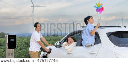 Concept Of Progressive Happy Family Enjoying Their Time At Wind Farm With Electric Vehicle. Electric