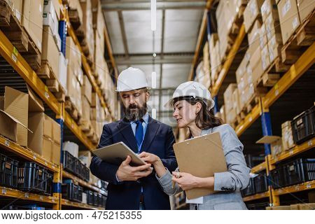 Managers In Suit Controlling Goods In A Waehouse.