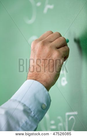 Closeup ของครูชายมือเขียนบน greenboard ในห้องเรียน