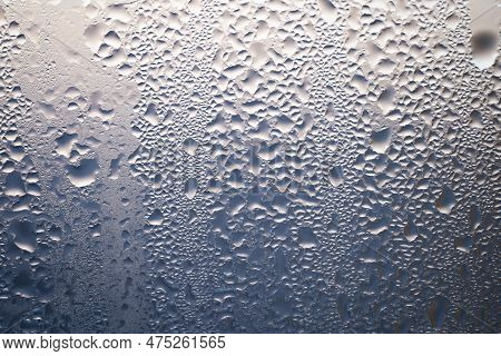 Backlit Chaotic Water Drops On Lightbeige And Blue Glass Background. Condensation After Rain Or Show