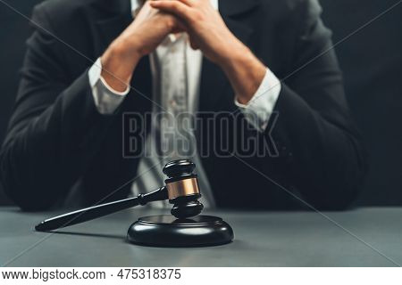 Focus Wooden Gavel Hammer With Burred Background Of Lawyer In Black Suit Sit On His Office Desk, Sym