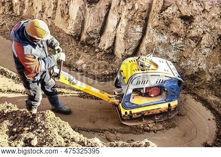 A Worker Compacts Soil Or Sand With A Vibrating Plate In A Trench At A Construction Site Close-up. V