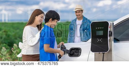 Concept Of Progressive Happy Family Enjoying Their Time At Wind Farm With Electric Vehicle. Electric
