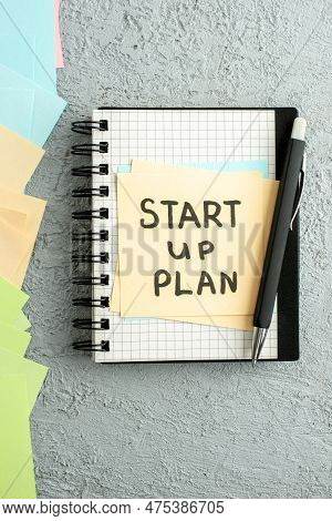 Vertical View Of Start Up Plan Writings On Sheet On Spiral Notebook On Black Book And Coloured Envel