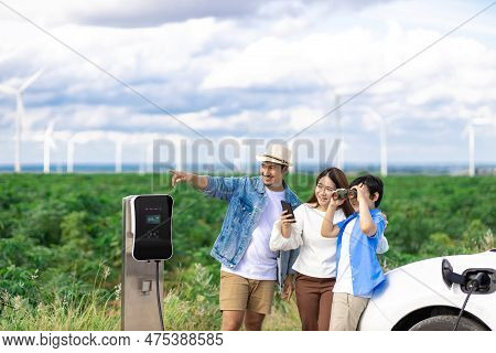Concept Of Progressive Happy Family Enjoying Their Time At Wind Farm With Electric Vehicle. Electric