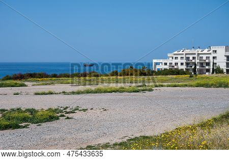 Melanos, Cyprus, March 25, 2023 - Gravel Beach, Grass And A Holiday Apartment Block In The Backgroun
