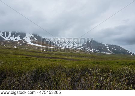 Dramatic Alpine Landscape With Snowy Mountains In Gray Low Clouds. Bleak Atmospheric Scenery Of Tund