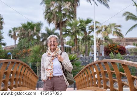 Happy Senior Woman Casual Dressed Walking On A Wooden Bridge Smiling Looking At Camera. Palm Trees O