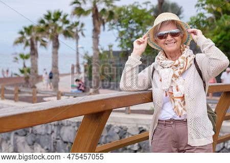 Portrait Of Happy Traveler Woman In Sea Vacation Holding His Summer Hat Looking At Camera Smiling.