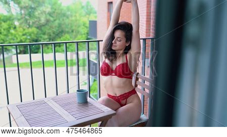 Beautiful Young Brunette Woman Sitting On Balcony In Red Lingerie And Drinking Coffee In The Morning