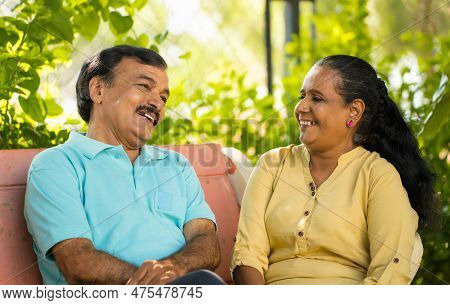 Happy Indian Senior Couple Talking Each Other While Sitting At Park - Concept Of Relaxation, Convers