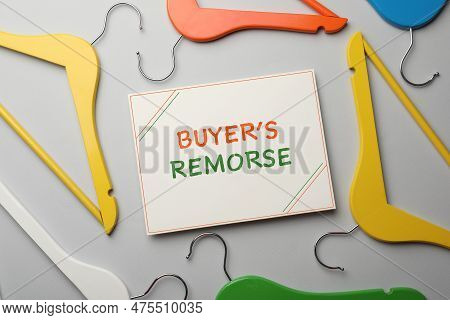 Card With Text Buyer's Remorse And Different Colorful Hangers On Light Grey Background, Flat Lay