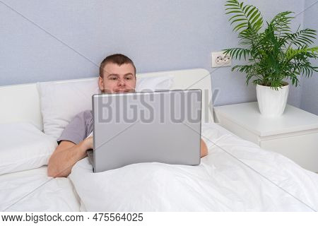 A Man With Laptop Is Lying In Bed. Freelancer Works Remotely From Home. Distance Education. Online S
