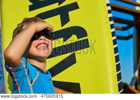Little Caucasian Boy In Sunglasses Closed His Eyes From The Bright Sun With His Hand, Looking Up At 