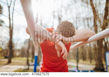 Exhausted Guy In Red T-shirt Collapsing After A Rigorous Parallel Bars Workout. A Tired Young Athlet