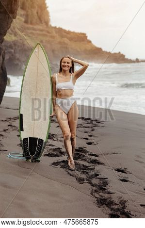 Healthy Smiling Fit Woman In Bikini Stands With Surfboard, On Black Beach By The Ocean. Extrime Wate