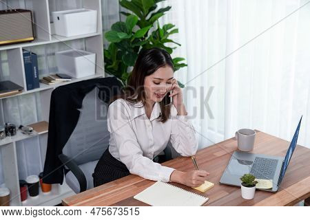 Young Enthusiastic Businesswoman Talking On Business Call And Writing Notes On Her Laptop As Multita