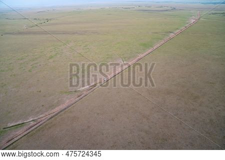 Very High Aerial View Of The Masaai Mara Reserve In Kenya During Sunrise. Safari Van Drives On The D