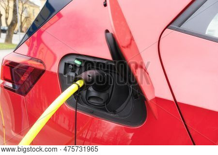 A Red Car With A Black Roof And A Yellow Electric Cable Stuck In It.