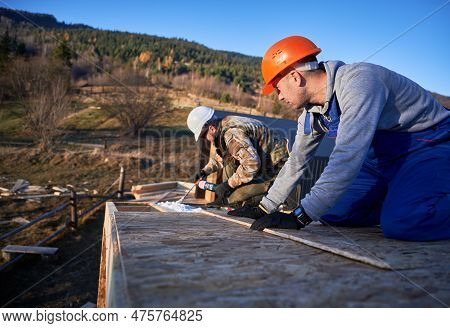 Male Builder Doing Thermal Insulation On Roof Of Wooden Frame House. Man Worker Spraying Polyurethan