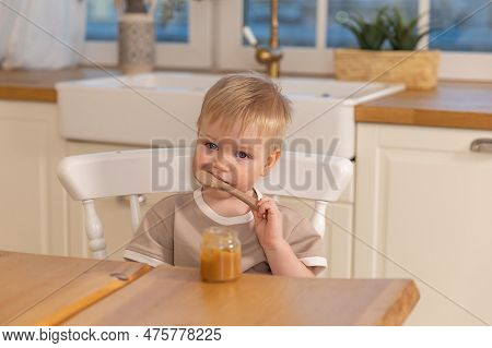 Happy Family At Home. Baby Boy Feeding Himself In Kitchen. Little Boy With Messy Funny Face Eats Hea