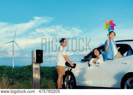 Concept Of Progressive Happy Family Holding Windmill Toy And Relax At Wind Farm With Electric Vehicl