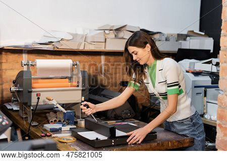 Cheerful Typographer Using Paper Trimmer Next To Print Plotter In Print Center.