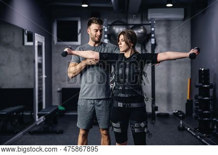 Electrical Muscle Stimulation Training Concept And Ems Suit. Male Coach In Grey Sportswear Helping A