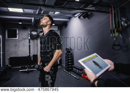 Portrait Of A Body Part Of A Man In A Black Ems Training Suit Standing In The Middle Of The Gym. He 