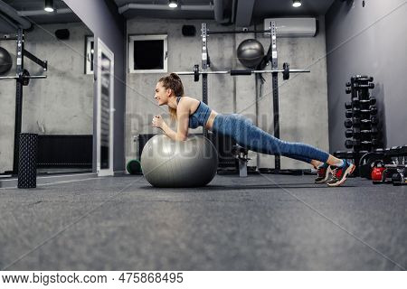 Plank Position Elbows Resting On A Fitness Ball. A Fit And Slim Woman In Sportswear Does Exercises T