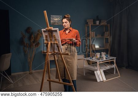 Portrait Of A Beautiful Female Artist, Stands Alone In A Modern Workshop, Paints A Picture On Canvas