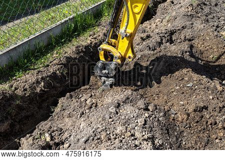Mini Digger Digging A Hole In The Garden Along The Fence To The Drainage Pipes.