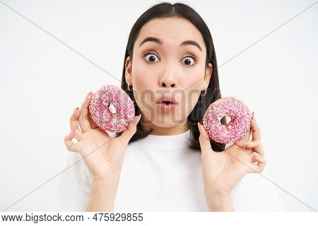Close Up Of Girl With Amazed Face, Shows Two Glazed Doughnuts, Tempted To Try New Delicious Donnut, 