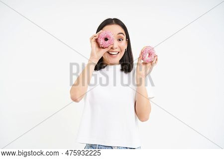 Beautiful Young Woman Eating Delicious Glazed Dougnuts, Holding Two Pink Donuts And Smiling, White B
