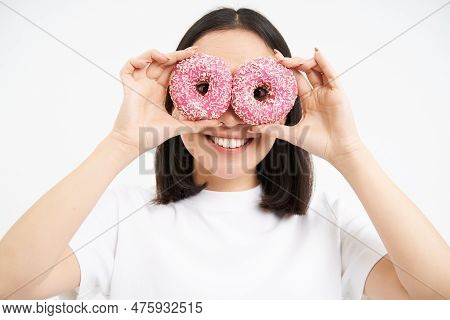 Image Of Funny Young Woman, Makes Glasses With Two Pink Glazed Doughnuts, Looking Through Donnut Hol