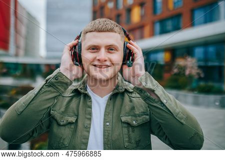 A Young Man With Headphones On, Looking Up At The City Skyline And Smiling As He Listens To His Favo