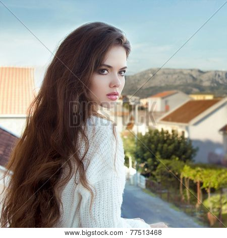 Attractive Brunette Girl With Healthy Long Wavy Hair Standing On Balcony Looking Away