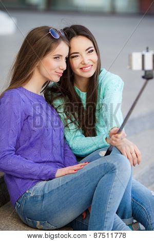 Two young attractive women are photographed with a smartphone on the streets.