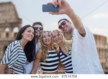 summer, europe, tourism, technology and people concept - group of smiling friends taking selfie with smartphone over coliseum background