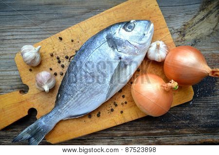 Uncooked fish dorado with garlic and onion
