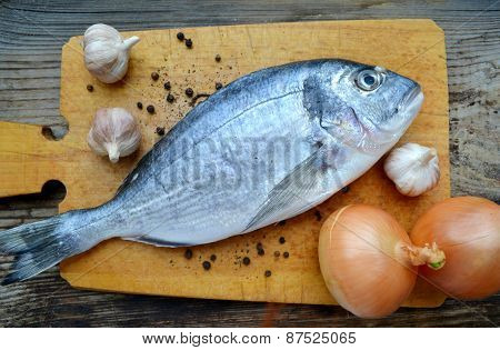 Uncooked fish dorado with garlic and onion